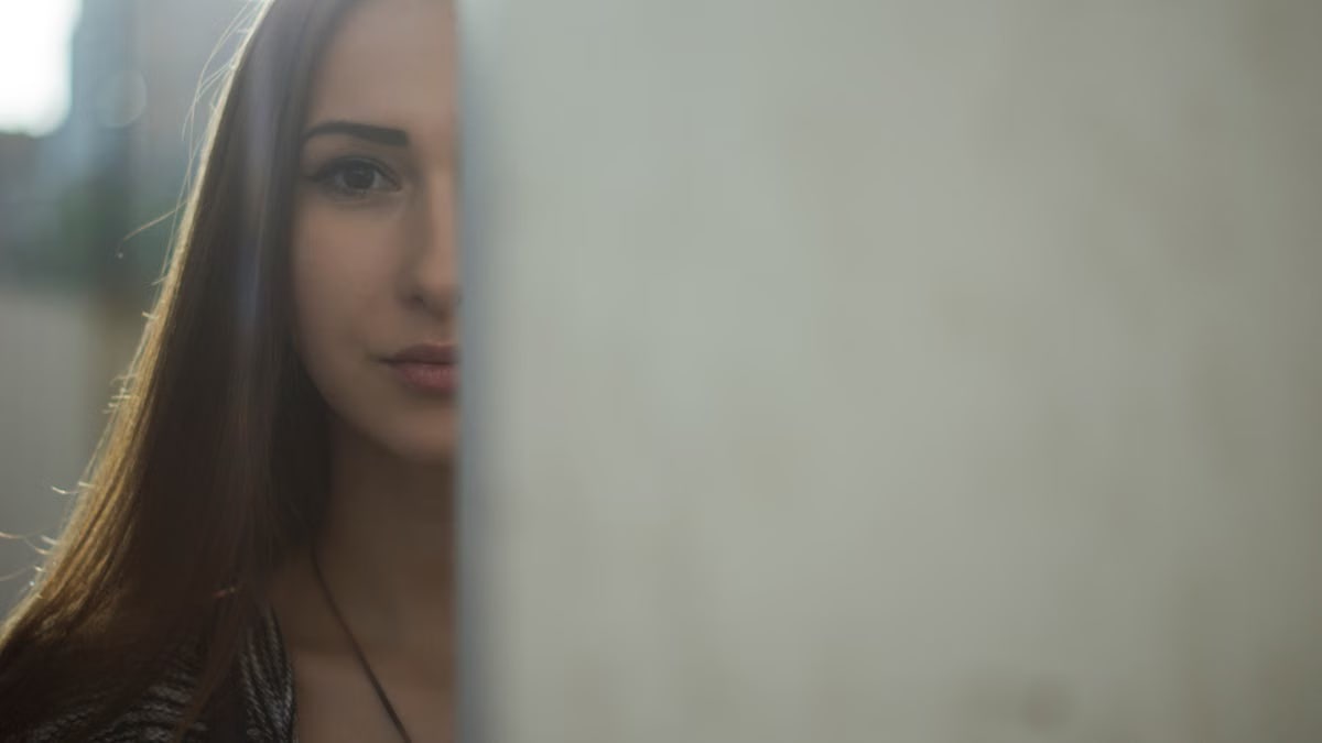 A mysterious and captivating portrait of a young woman partially hidden behind a soft focus background.